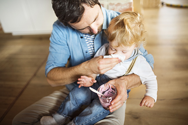 Young father at home feeding his little son with yoghurt.
